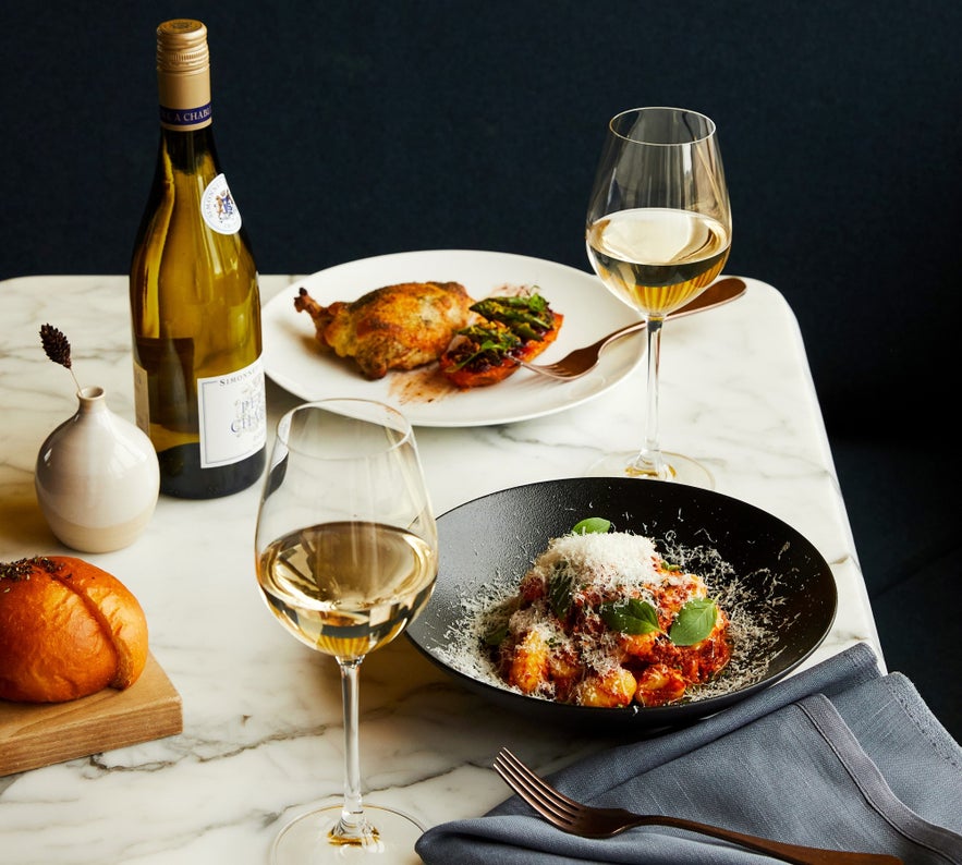 Elegant dining setup at Tides Restaurant in Reykjavik, featuring gnocchi, roasted chicken, fresh bread, and white wine.