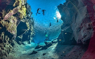 Snorkelers floating between the North American and Eurasian tectonic plates in crystal-clear Silfra Fissure water.