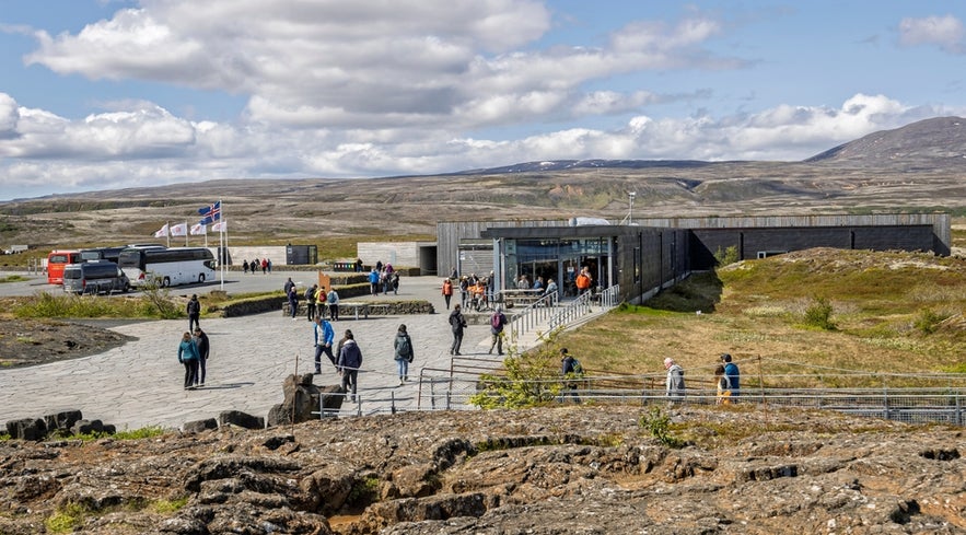 Visitors at Thingvellir National Park Visitor Center in Iceland with tour buses and mountain views in the background.