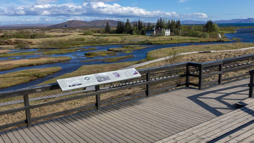 Gangbro gjennom Almannagja-kløften i Thingvellir nasjonalpark med utsikt mot elven Oxara og Thingvellir kirke.