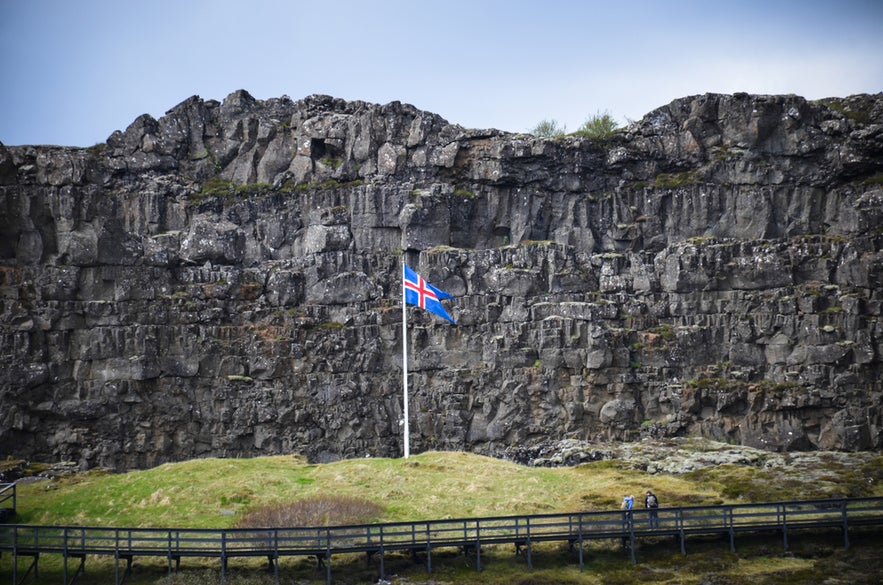 Almannagja Gorge Boardwalk at Thingvellir National Park with Logberg Law Rock and Icelandic flag.