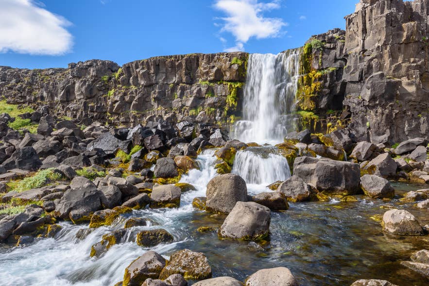 Oxararfoss Waterfall in Thingvellir National Park, Iceland, flowing over volcanic cliffs into a rocky stream.