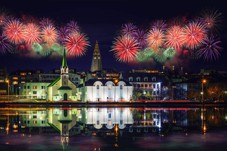 Fuochi d'artificio su Reykjavik con la chiesa Hallgrimskirkja e Frikirkjan riflesse nello stagno Tjornin, una scena festosa durante il Natale in Islanda.