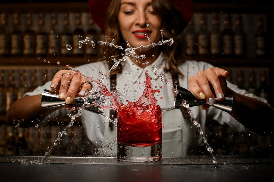 Bartender mixing a bright red drink with splashes, highlighting the energy of cocktail bars in Reykjavik.