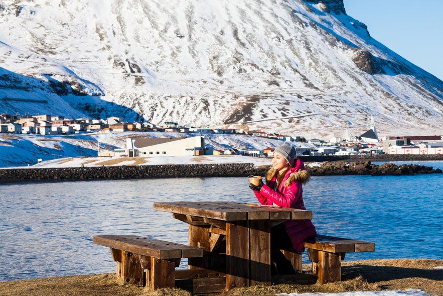 Woman enjoying a hot cup of coffee in Olafsvik, Iceland, during winter snow.