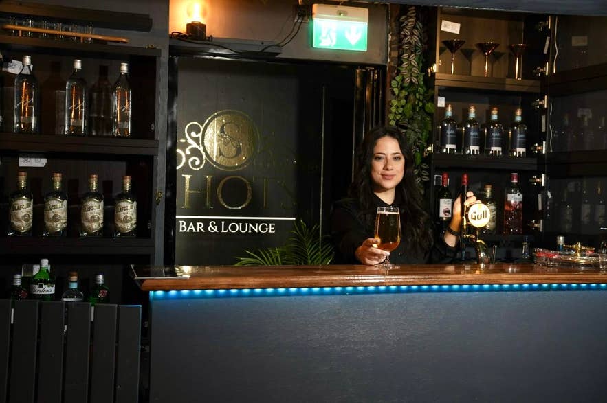 一名女子站在Shots Bar&Lounge的吧台后，这家热门哈夫纳夫约杜尔酒吧以热闹的卡拉OK之夜闻名。