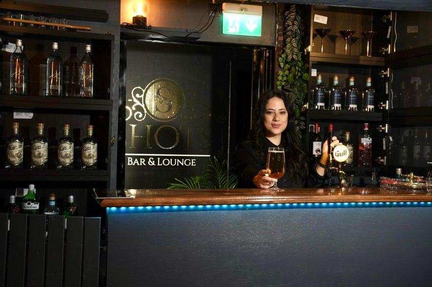 A woman stands behind the bar at Shots Bar&Lounge, a popular Hafnarfjordur bar known for its lively karaoke nights.
