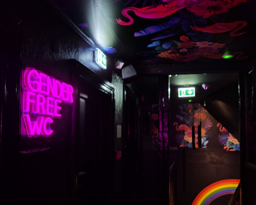 Gender-free restroom sign in neon at Kiki Bar Reykjavik with colorful wall art and rainbow details.