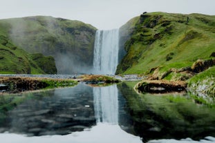 Skogafoss waterfall reflecting in a calm river on Iceland’s South Coast in summer