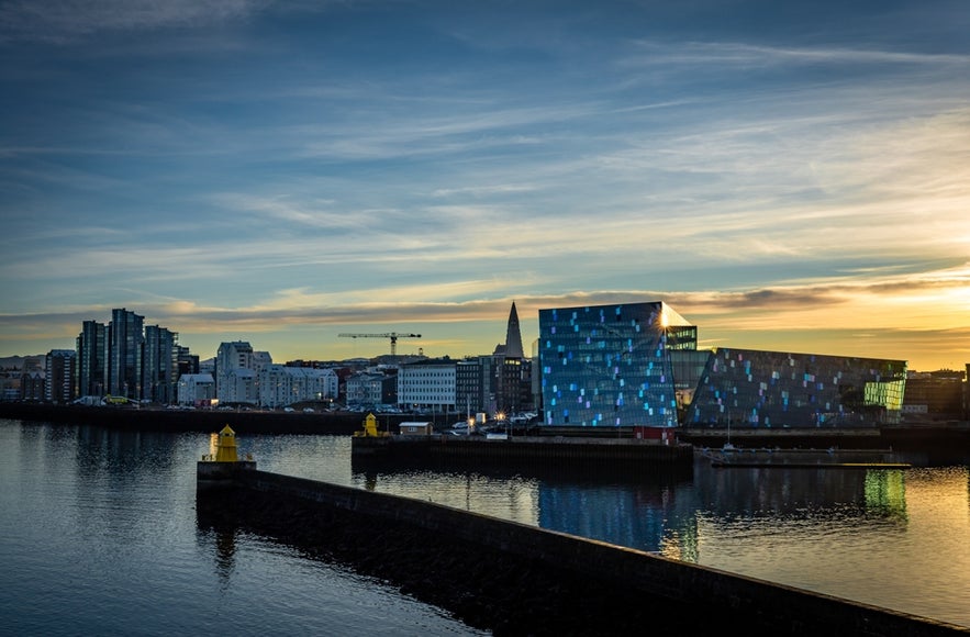 View of Harpa Concert Hall and downtown Reykjavik, Iceland, at sunset with reflections on the harbor water.