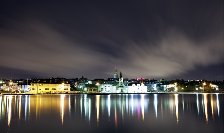 Night view of Reykjavik, Iceland, with Frikirkjan church and city lights reflecting on Tjornin Pond.