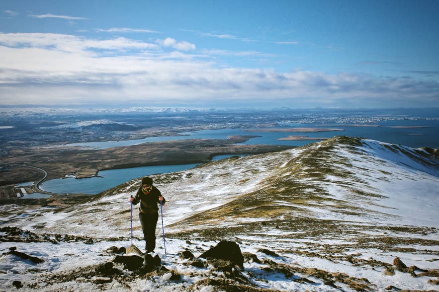 Hiker on snowy Mount Esja overlooking lakes and valleys.