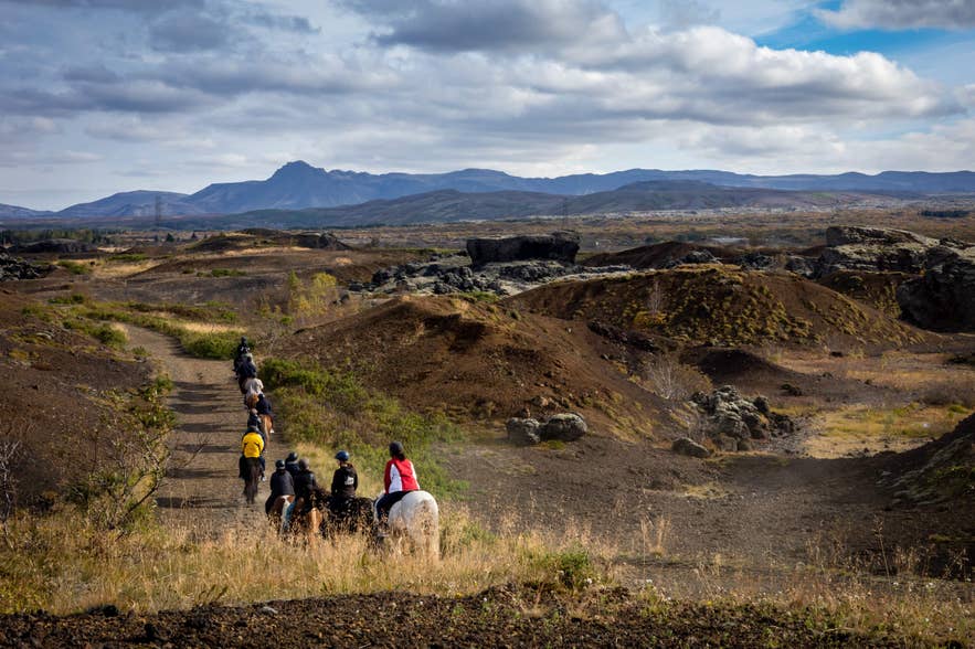Group horseback riding in Raudholar through a volcanic landscape with distant mountains.