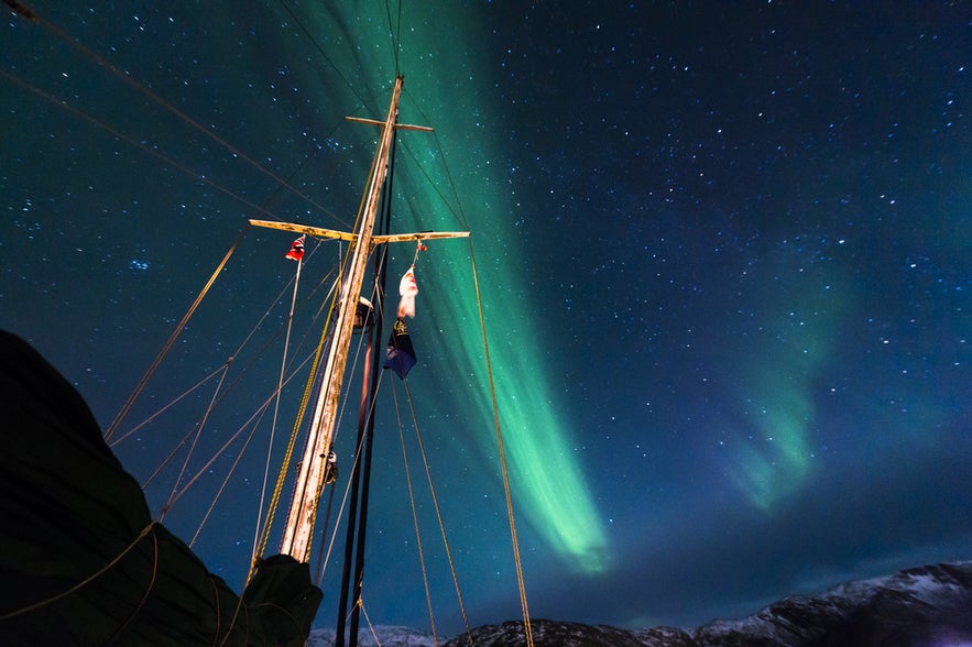 Aurora borealis above a sailboat and the starry night sky during a northern lights cruise in Reykjavik.