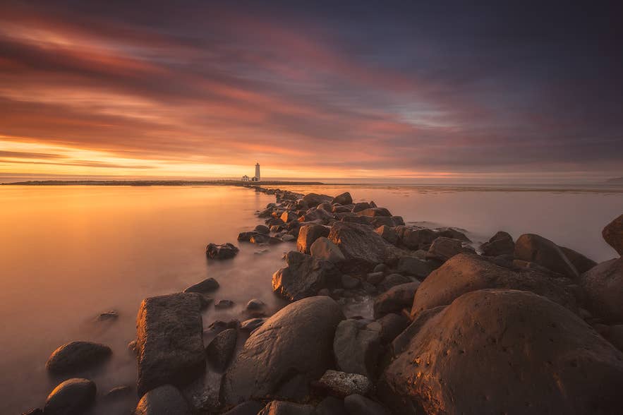 Rocky shoreline leading to Grotta Lighthouse during a dramatic sunrise.