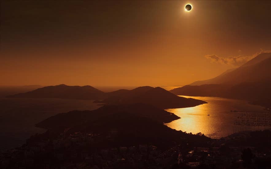 Total solar eclipse over the coastal mountains and golden water.
