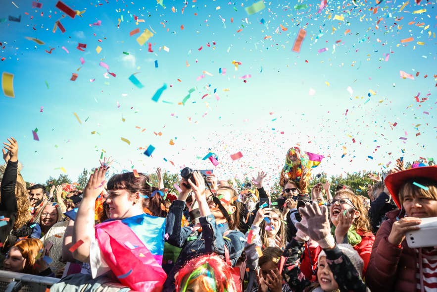 Een menigte viert buiten feest terwijl er regenboogconfetti door de lucht vliegt tijdens het Reykjavik Pride Festival.