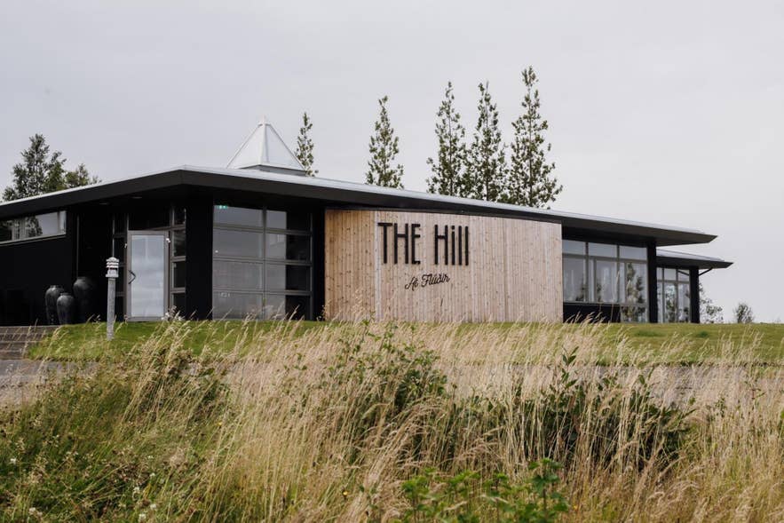 Exterior view of The Hill restaurant with wooden facade and large windows, set in Iceland’s scenic rural landscape.