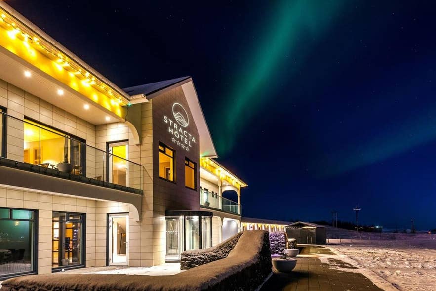 Stracta Hotel in Iceland lit up at night with northern lights glowing above in the winter sky. Stracta Hotel in Iceland lit up at night with northern lights glowing above in the winter sky.
