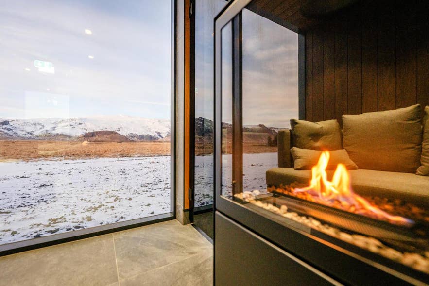 Acogedor salón de Umi Hotel con chimenea y vistas panorámicas de las montañas nevadas de Islandia a través de grandes ventanales.