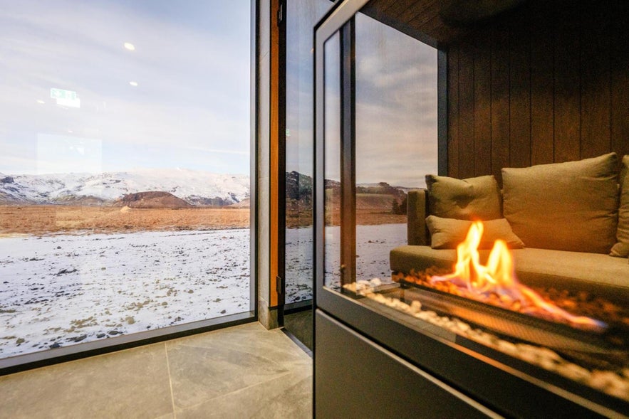 Cozy lounge at Umi Hotel with fireplace and panoramic views of Iceland’s snowy mountains through large windows. Cozy lounge at Umi Hotel with fireplace and panoramic views of Iceland’s snowy mountains through large windows.