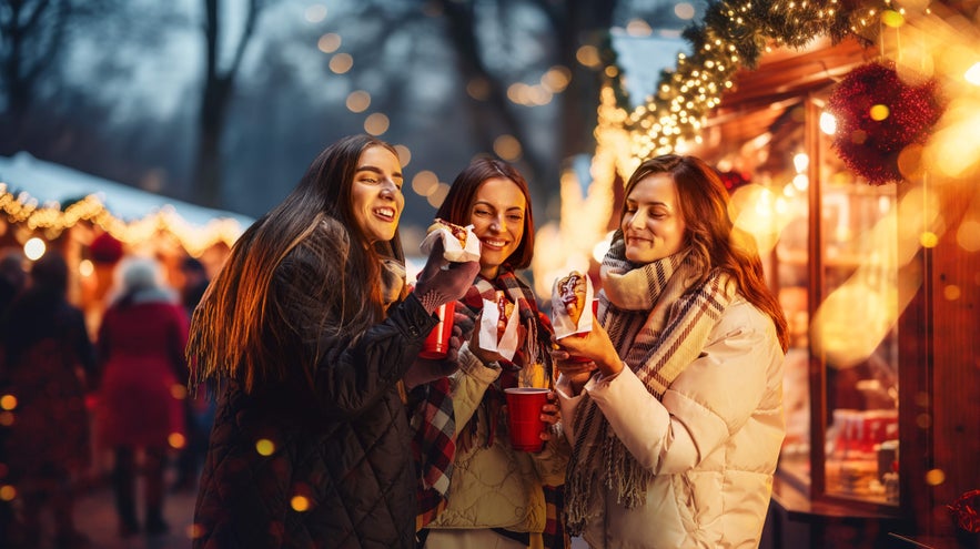 Friends enjoying food and drinks at a Reykjavik Christmas market with festive lights in the background