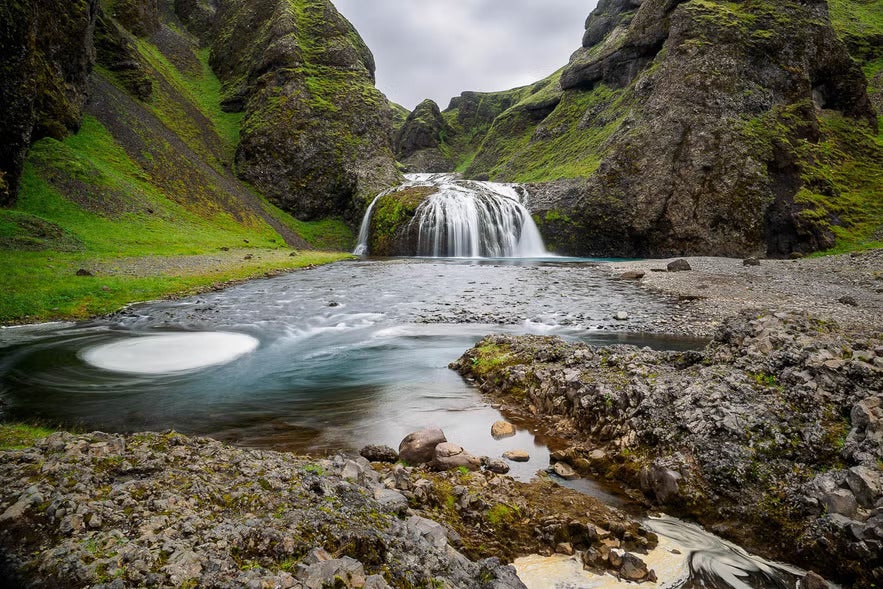 Stjornarfoss waterfall in South Iceland surrounded by mossy cliffs.