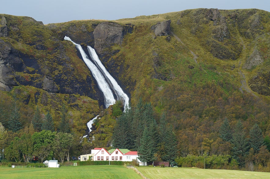 Systrafoss waterfall in South Iceland flowing down a mossy cliff beside a farmhouse.
