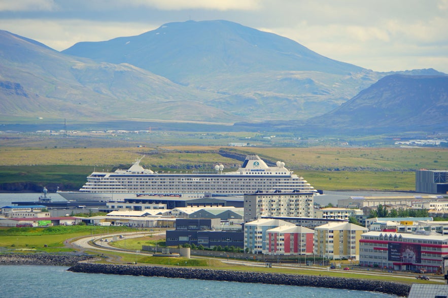 Large cruise ship docked in Reykjavik harbor with Icelandic mountains in the background on a partly cloudy day.