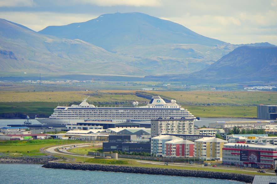 Grand navire de croisière amarré dans le port de Reykjavik, avec les montagnes islandaises en arrière-plan par une journée partiellement nuageuse.