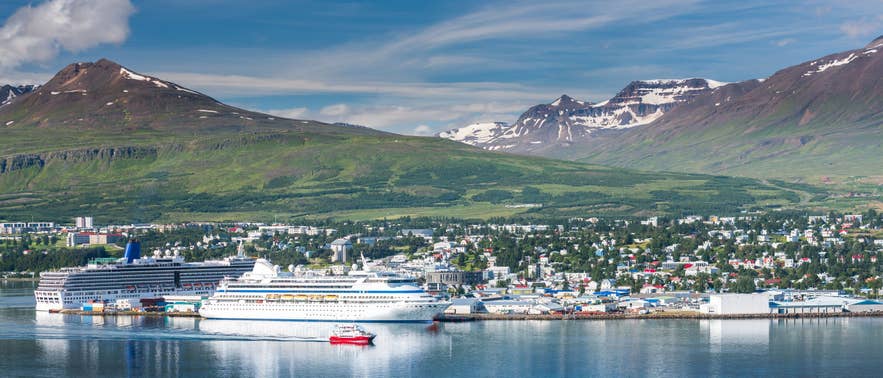 Deux navires de croisière amarrés dans le port d’Akureyri, avec des sommets montagneux et la ville sous un ciel estival dégagé.