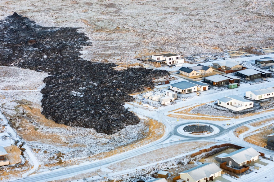 Aerial view of lava flow reaching homes in snowy Grindavik, Iceland, showing the impact of recent volcanic activity.