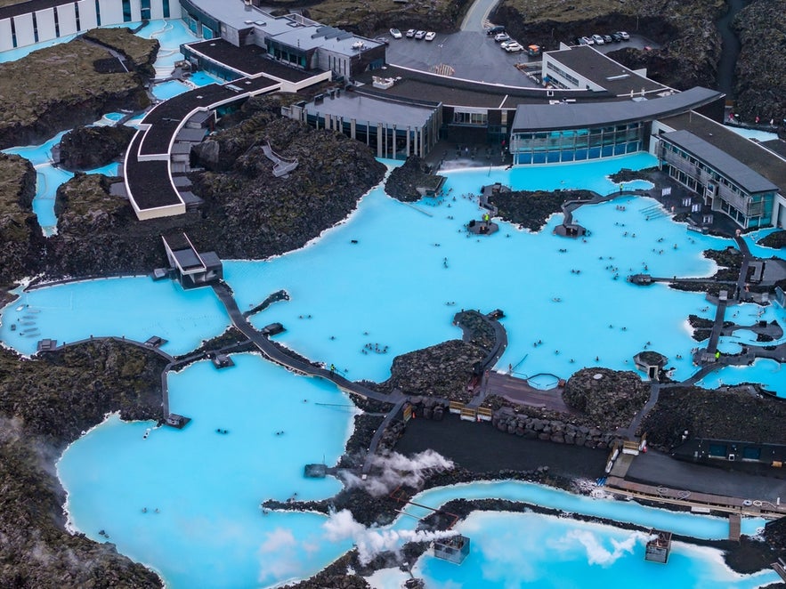 The Blue Lagoon Geothermal Spa in Iceland has milky-blue geothermal waters surrounded by dark lava rocks, with modern buildings close by.