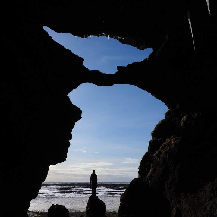 A person stands before Yoda Cave, one of the stops of the private Katla ice cave tour, forming a picture-perfect silhouette.