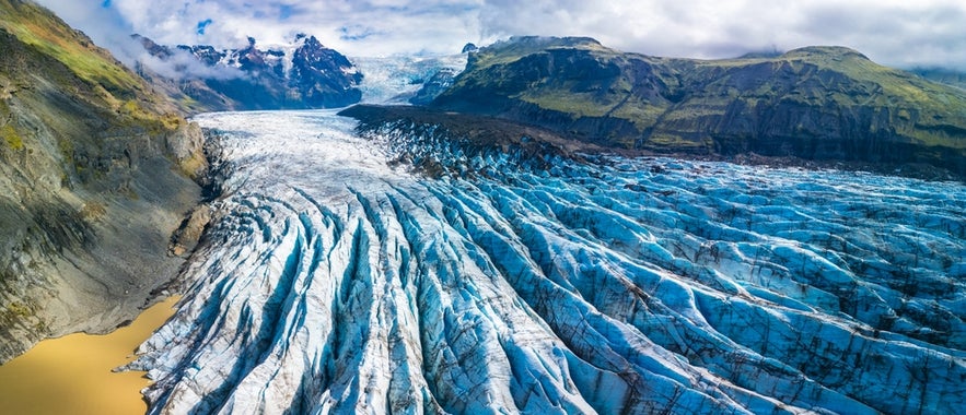 A panoramic view of Skaftafell Nature Reserve shows the rugged, icy surface of Svinafellsjokull Glacier stretching through the landscape, surrounded by mountains and valleys.