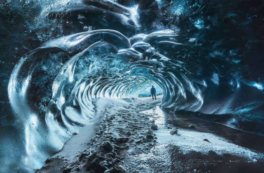 Persona che esplora una grotta di ghiaccio blu scintillante in Islanda, con pavimento innevato e pareti ghiacciate
