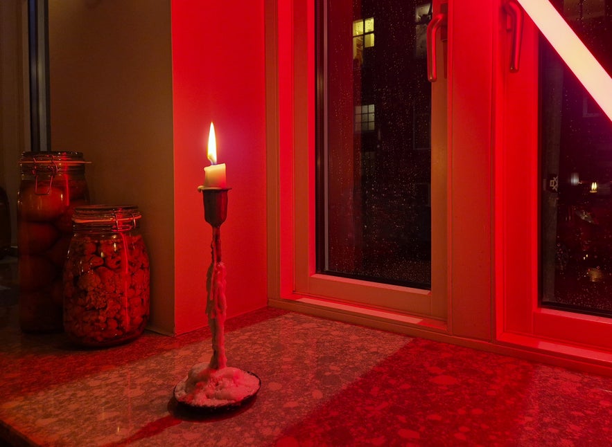 Candle burning on a windowsill with red lighting and glass jars inside Litli Barinn in Reykjavik.