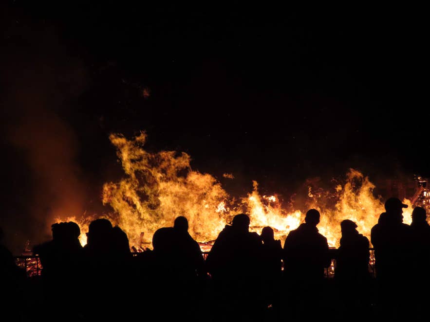 Sagome di persone che osservano un grande falò che arde contro il cielo notturno in Islanda