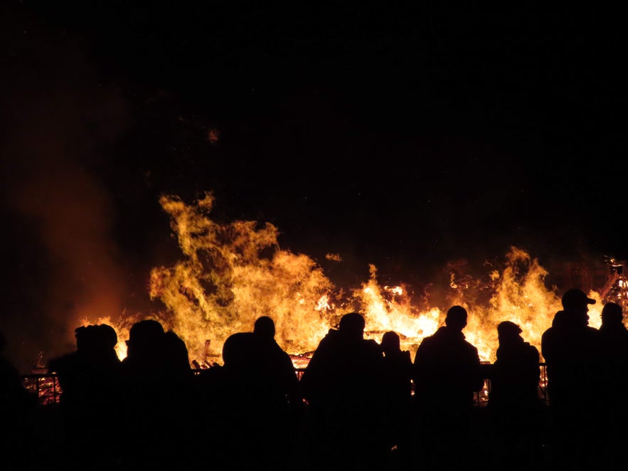 Silhouettes of people watching a large bonfire blaze against the night sky in Iceland