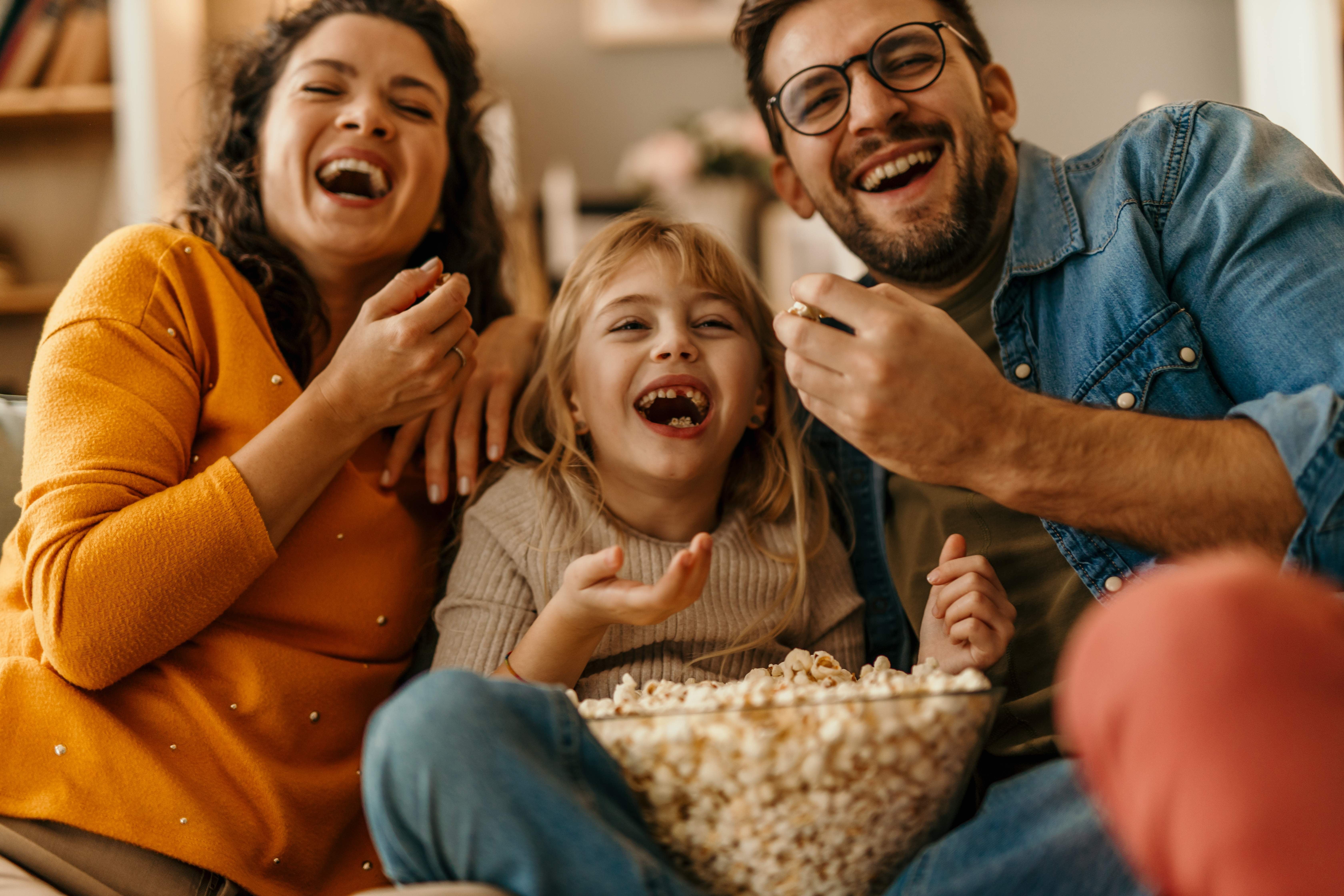 Happy family laughing together while watching a comedy in Iceland and sharing a big bowl of popcorn