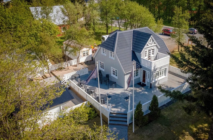 Aerial view of Nielsen Restaurant in Egilsstadir, housed in a historic grey wooden building with a large outdoor terrace surrounded by trees.