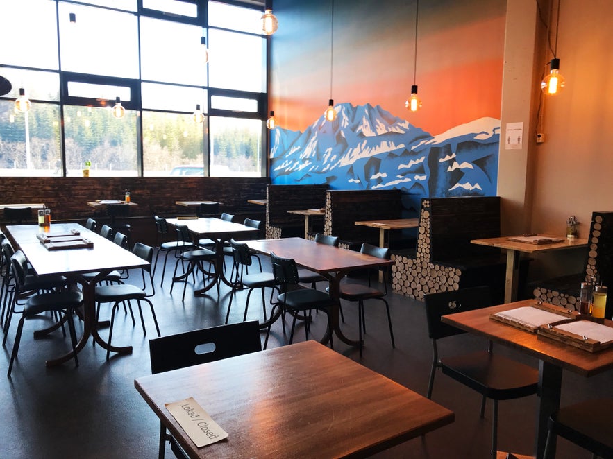 Interior of Askur Taproom & Pizzeria in Egilsstadir, with wooden tables, black chairs, and booth seating decorated with a mountain mural and log-style details.