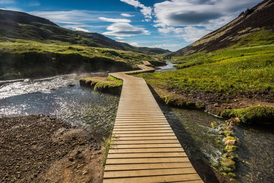 La zone de sources chaudes naturelles de Reykjadalur, avec un pont en bois au-dessus d’une rivière fumante, est un site pittoresque à visiter lors d’un week-end en Islande.