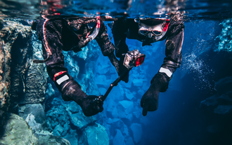 2 snorkelers swim in clear waters in the Silfra Fissure equipped with an underwater camera.