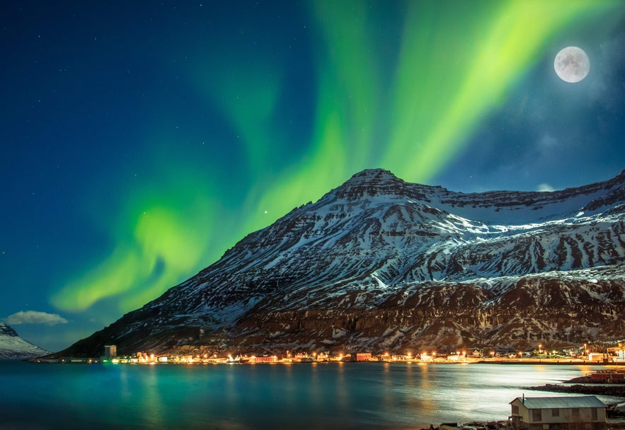 Bright northern Lights and full moon above Seydisfjordur's mountains and harbor in January in Iceland