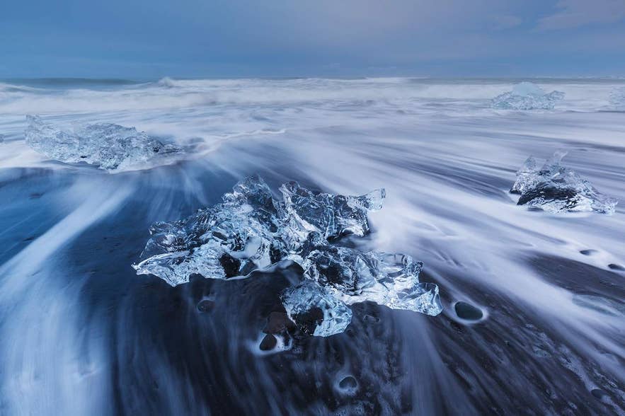 ダイヤモンドビーチの黒砂の上で輝く氷塊。1月のアイスランドで波が氷を包み込む幻想的な光景