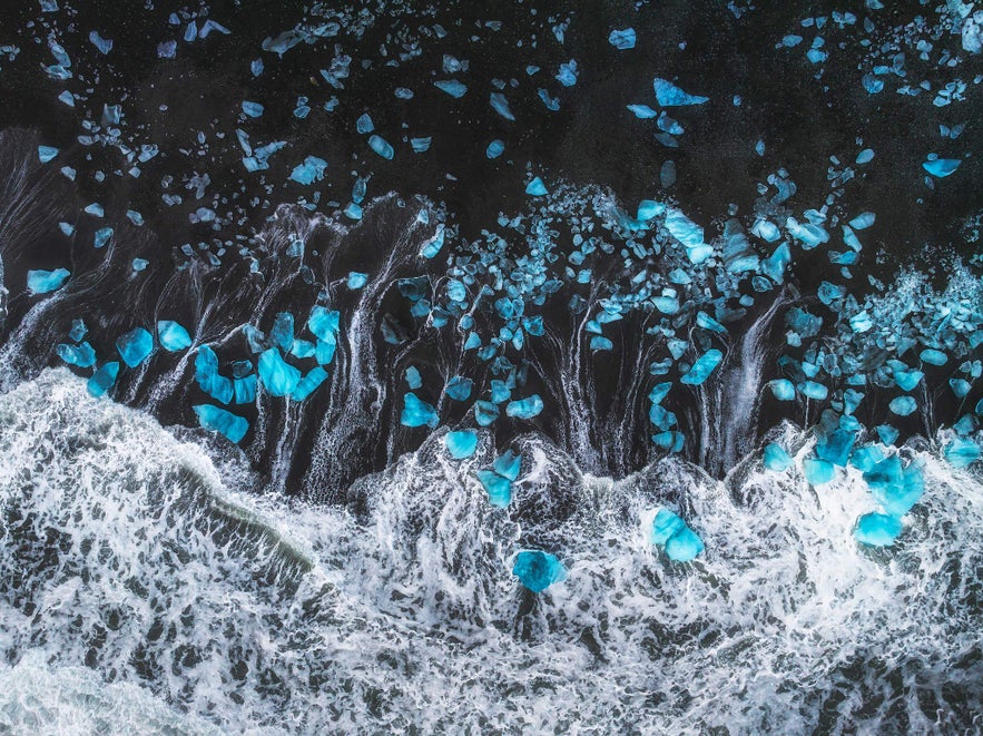 Aerial view of blue ice chunks scattered along Diamond Beach’s black sand shore in Iceland in January Aerial view of blue ice chunks scattered along Diamond Beach’s black sand shore in Iceland in January