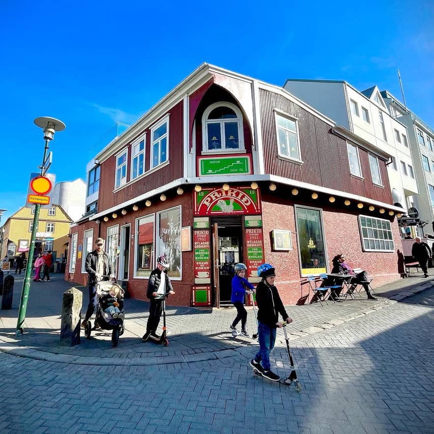 People walk and play outside Prikið café on Laugavegur Street in Reykjavik under a bright blue sky.