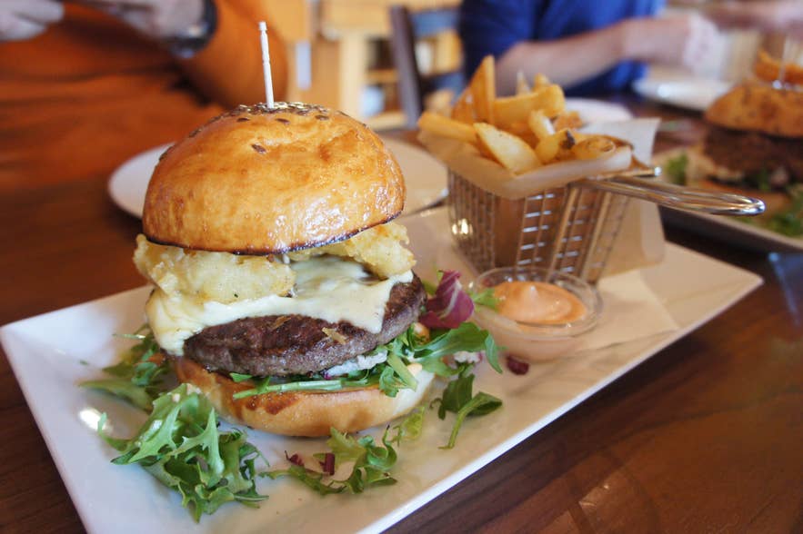 Cheeseburger with crispy onion rings, melted cheese, and fries served at a restaurant in Reykjavik.