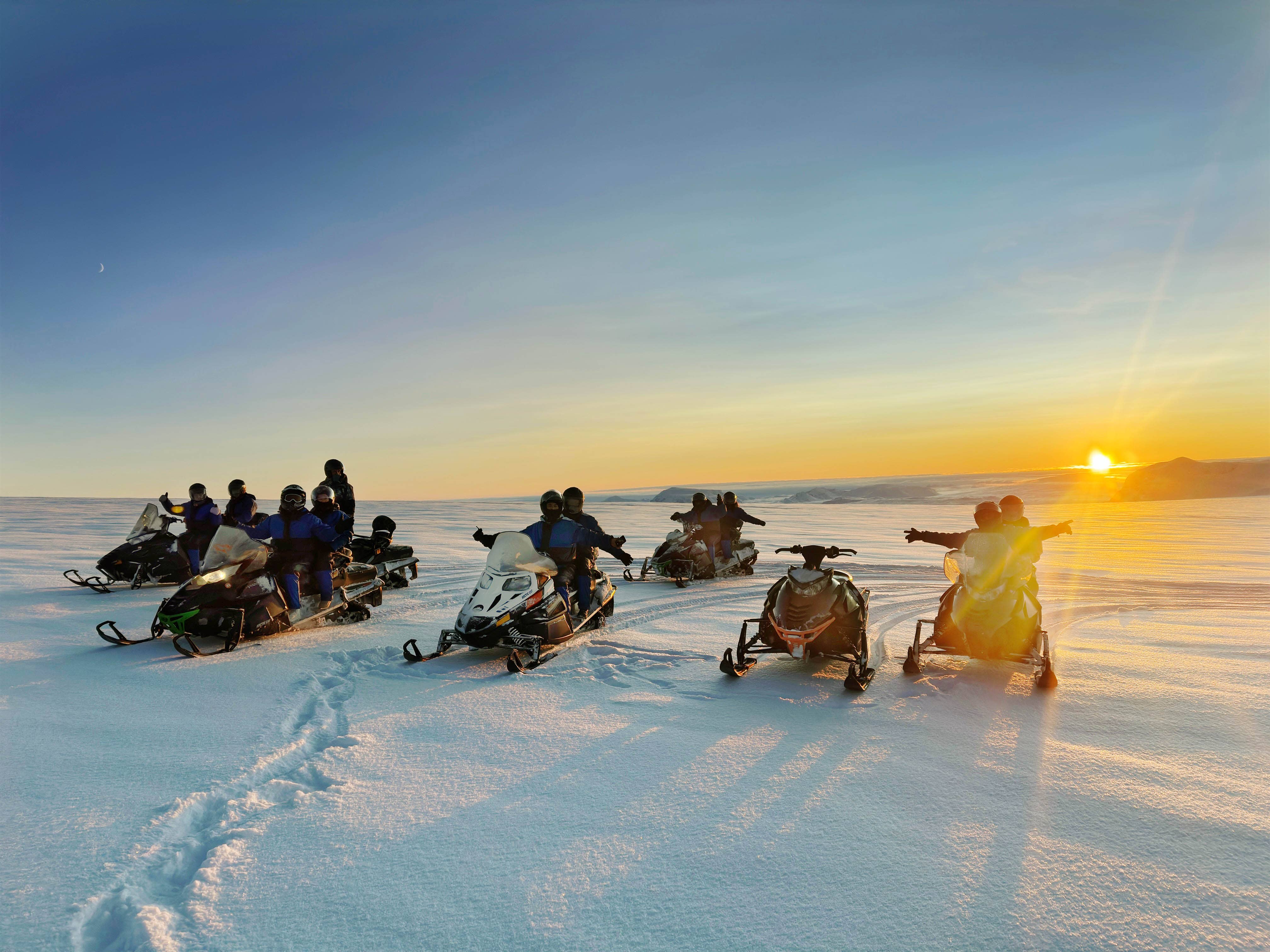 Snowmobilers ride across Langjokull Glacier at sunset during a snowmobile tour.